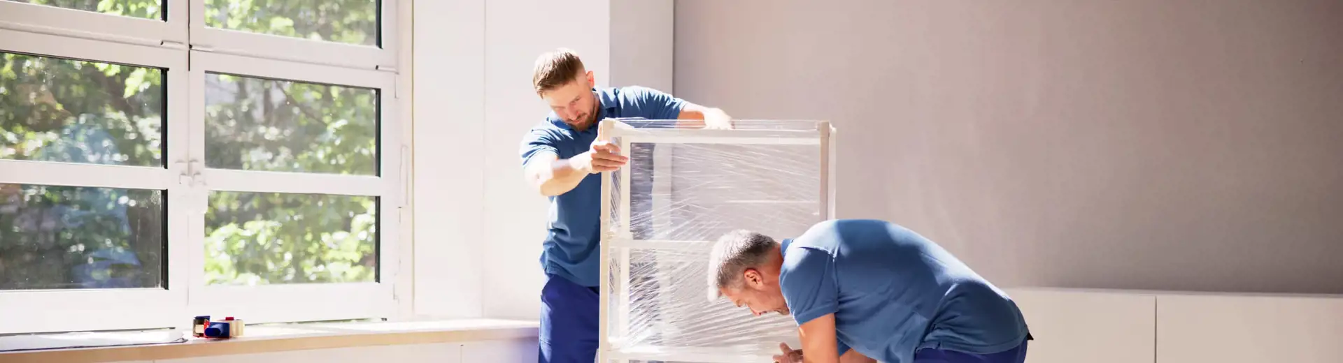 two movers in blue uniforms wrapping furniture for a move