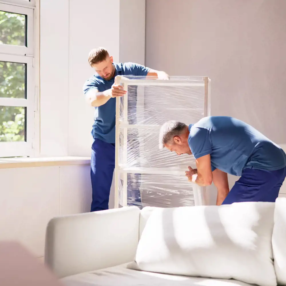 two movers in blue uniforms wrapping furniture for a move
