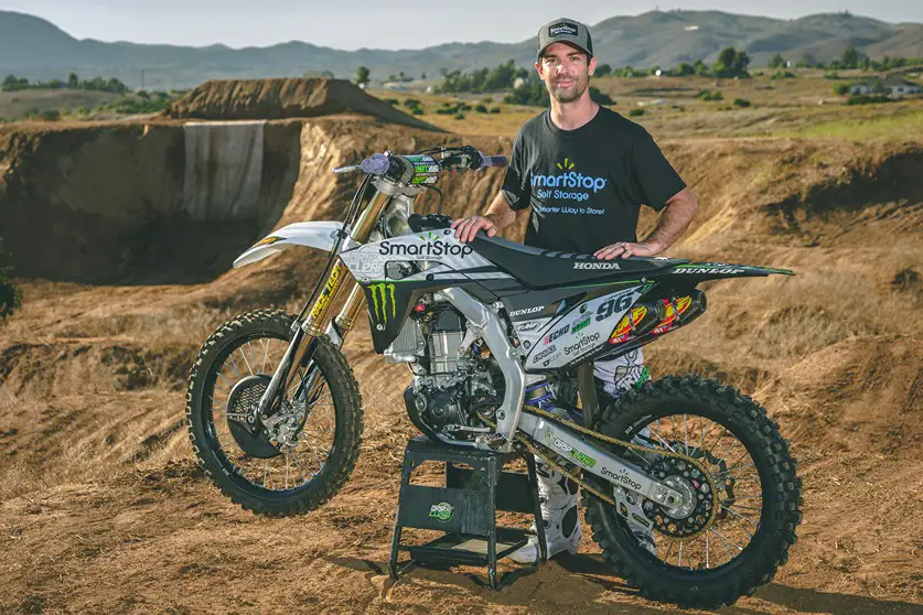 Bryce Hudson pose avec son motocross près d'un circuit de terre battue
