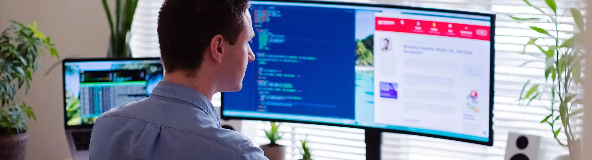 Un homme assis à un bureau face à une fenêtre, utilisant une souris avec plusieurs moniteurs affichant différents écrans devant lui.
