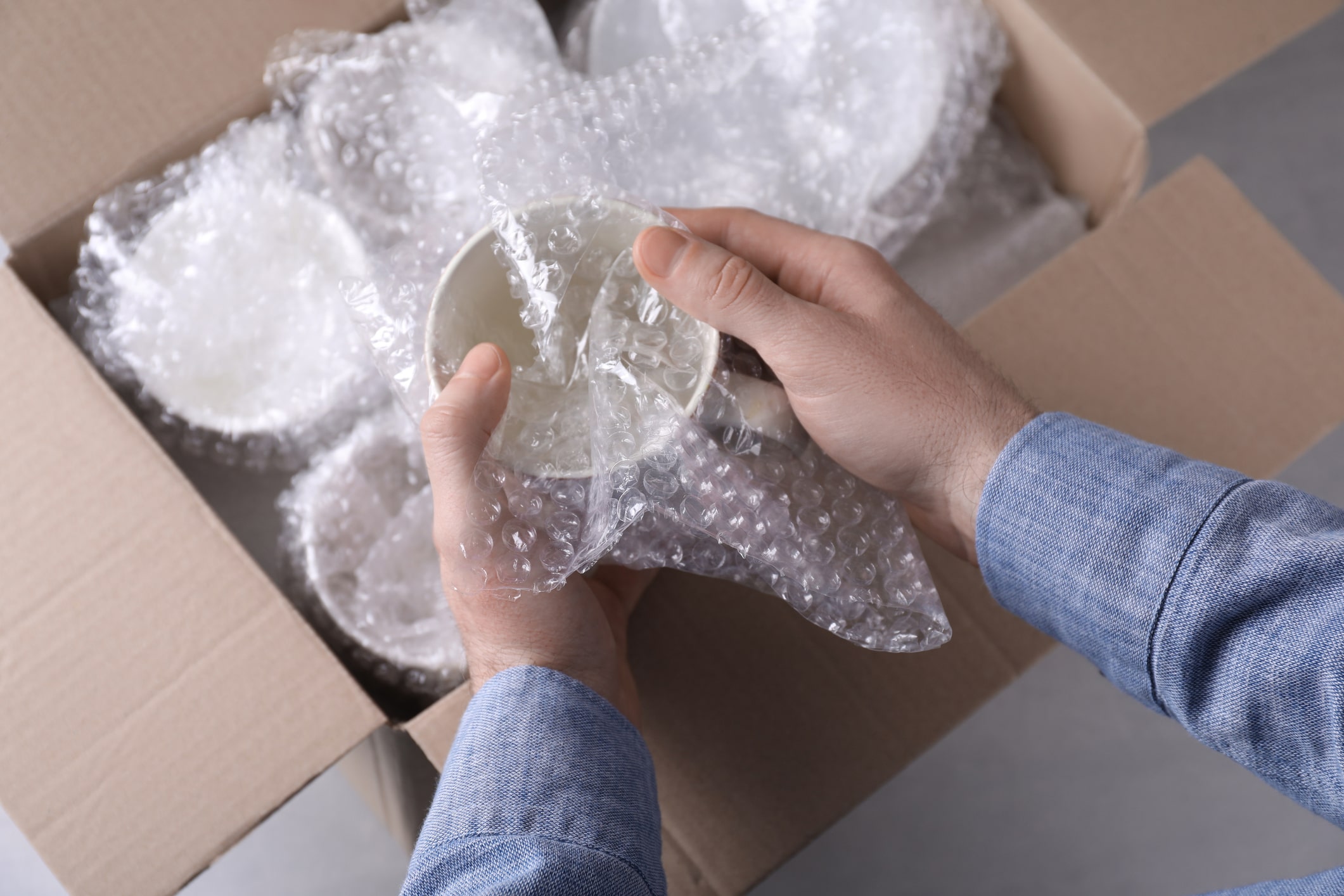 person wrapping delicate china in bubble wrap