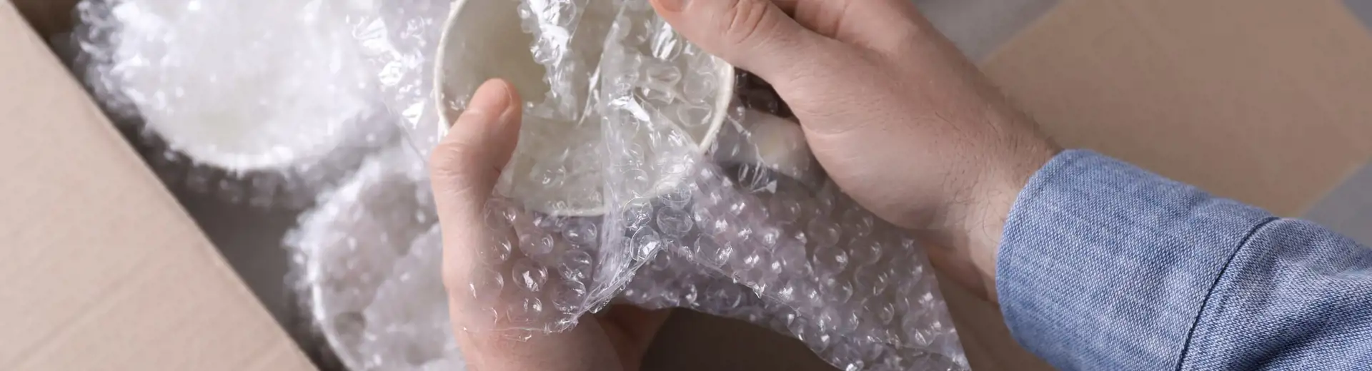 person wrapping delicate china in bubble wrap