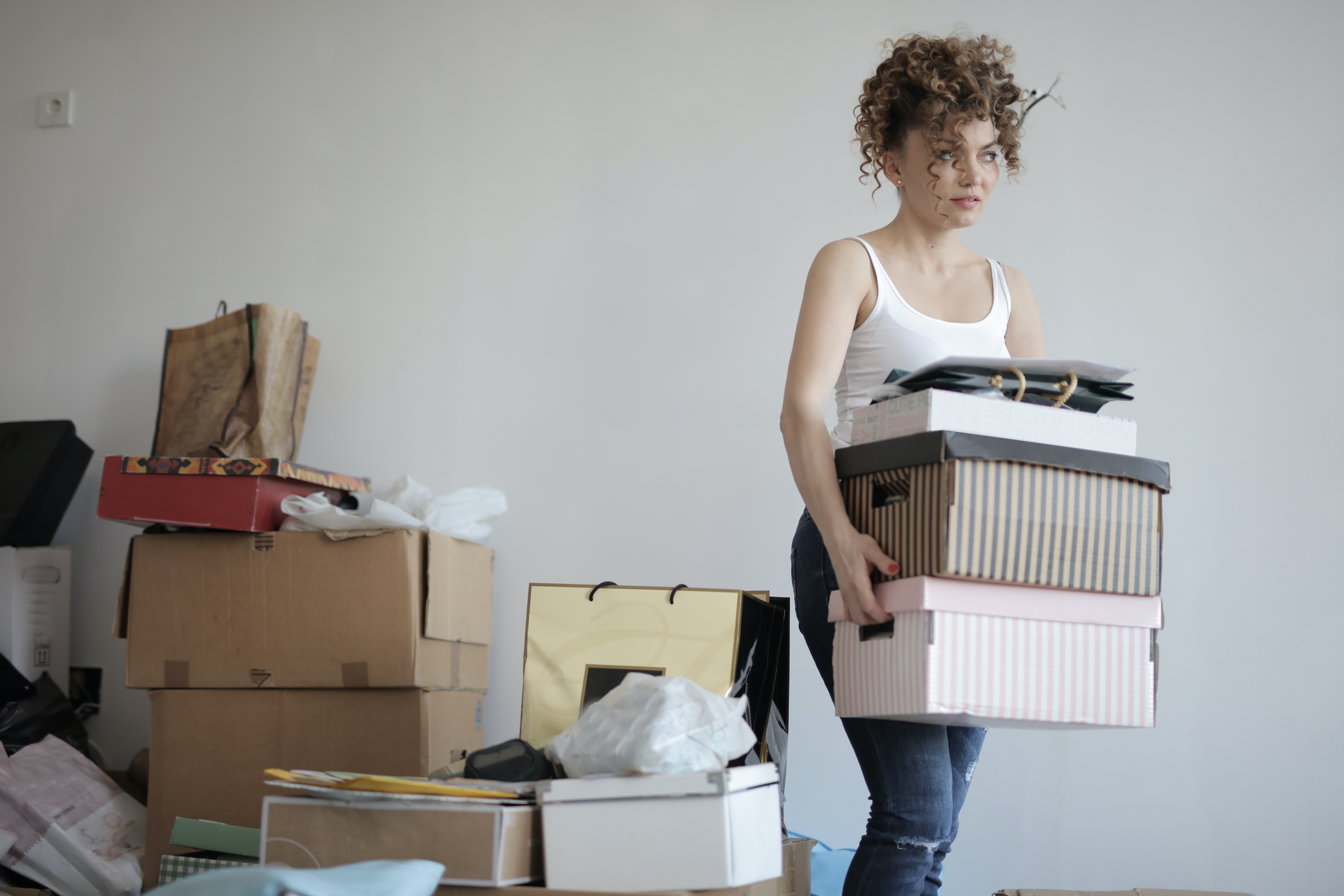 A woman carrying some boxes with others laying on the floor in her room.