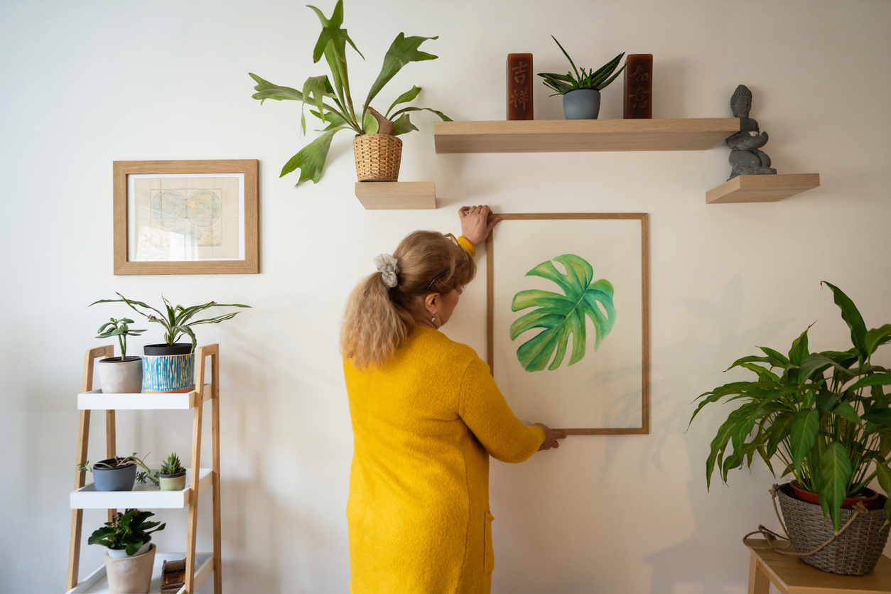 woman adding an art piece of a monstera leaf to her wall
