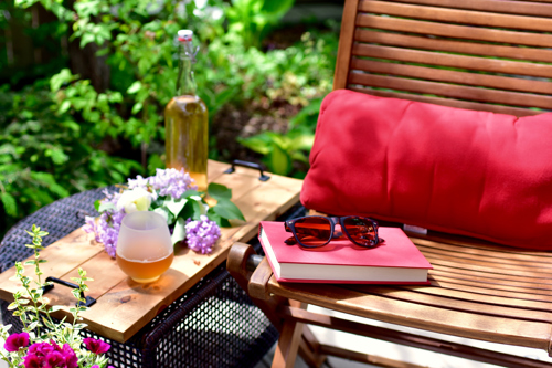 hardback book, sunglasses, wine, and flowers in a backyard reading nook