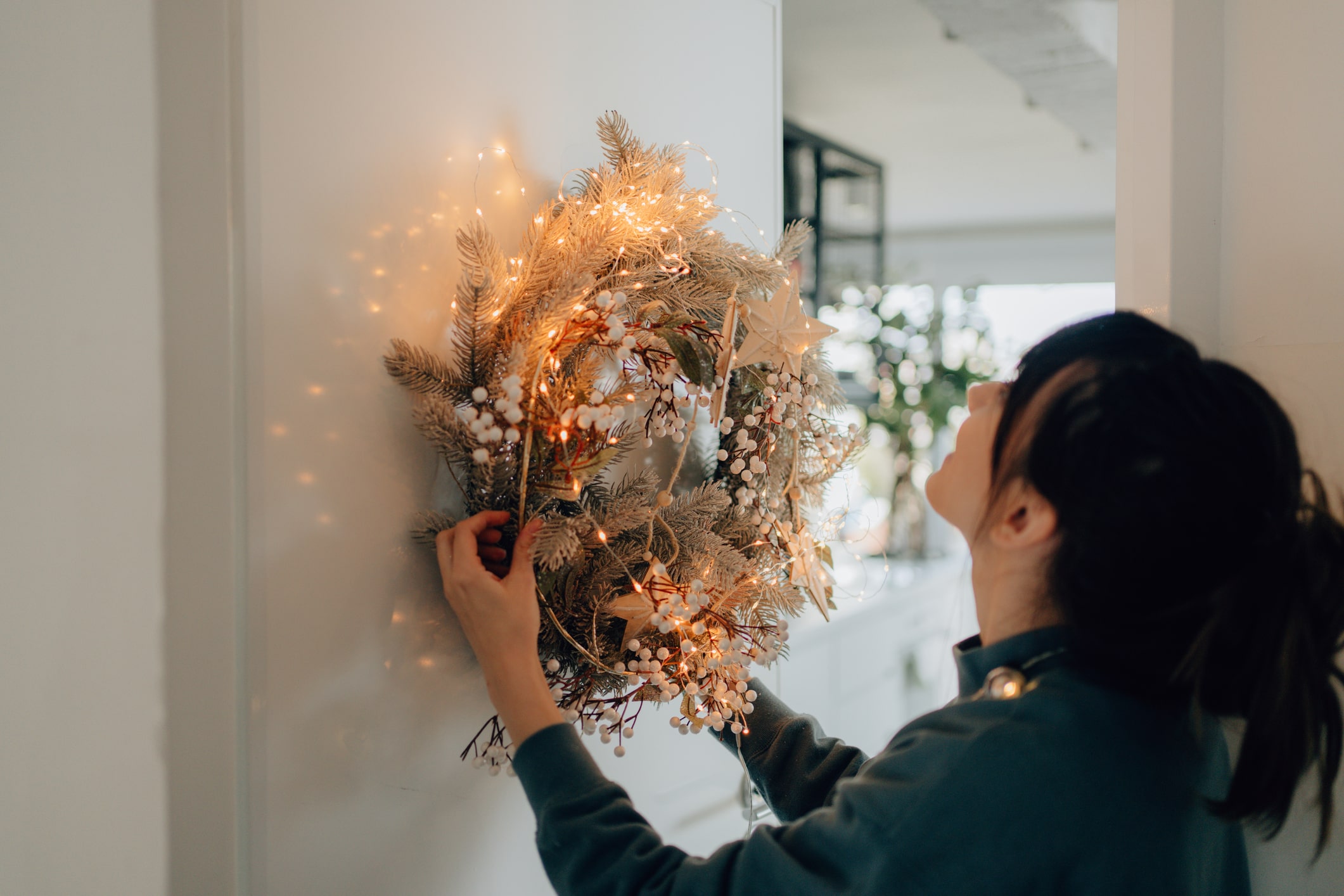 woman hanging holiday wreath with led lights and flowers on wall