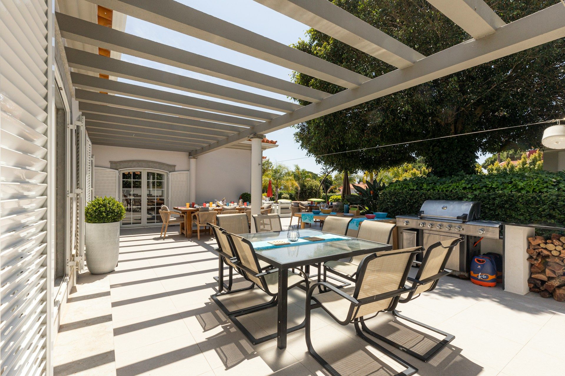 sunny backyard patio with outdoor grill and glass dining table and furniture